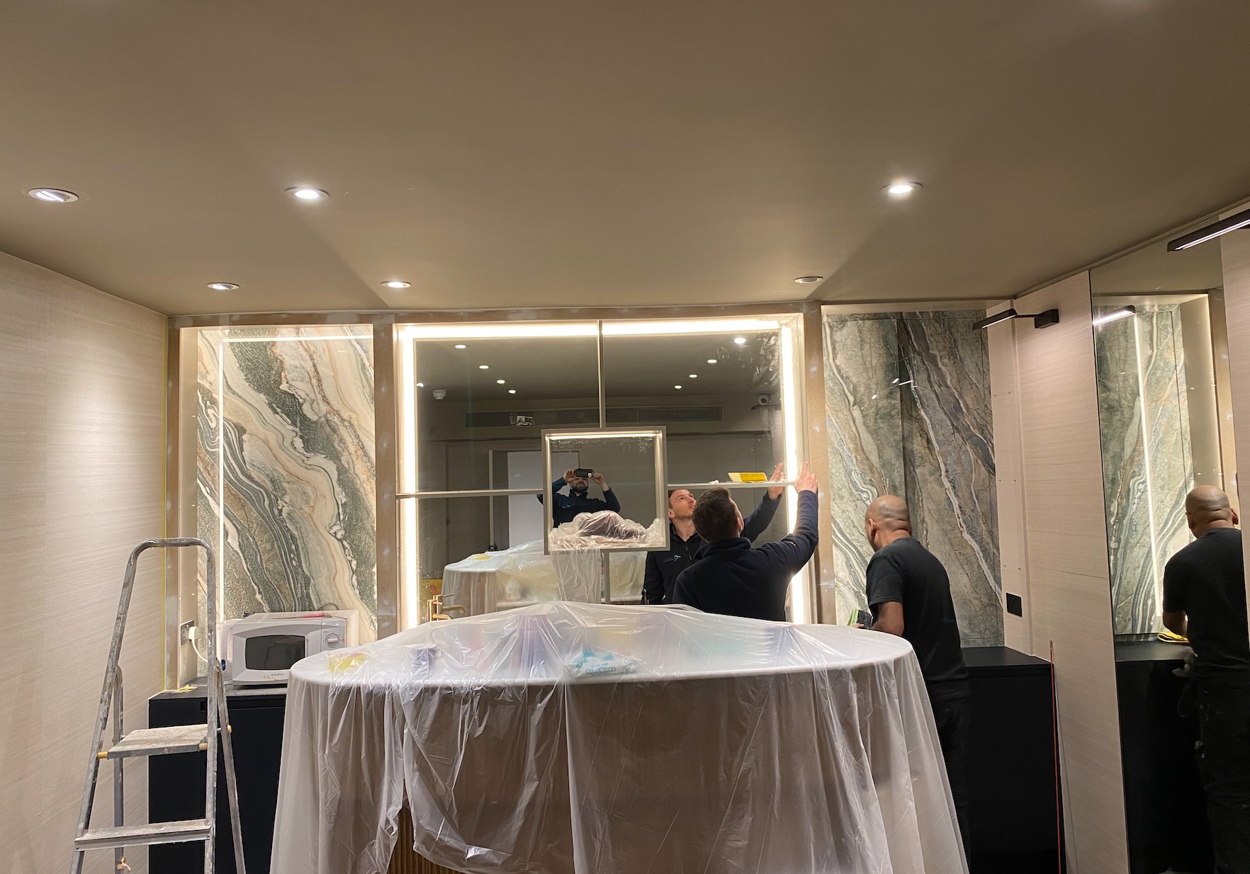 Marble bathroom with a backlit mirror and lit vanity being finished by the team